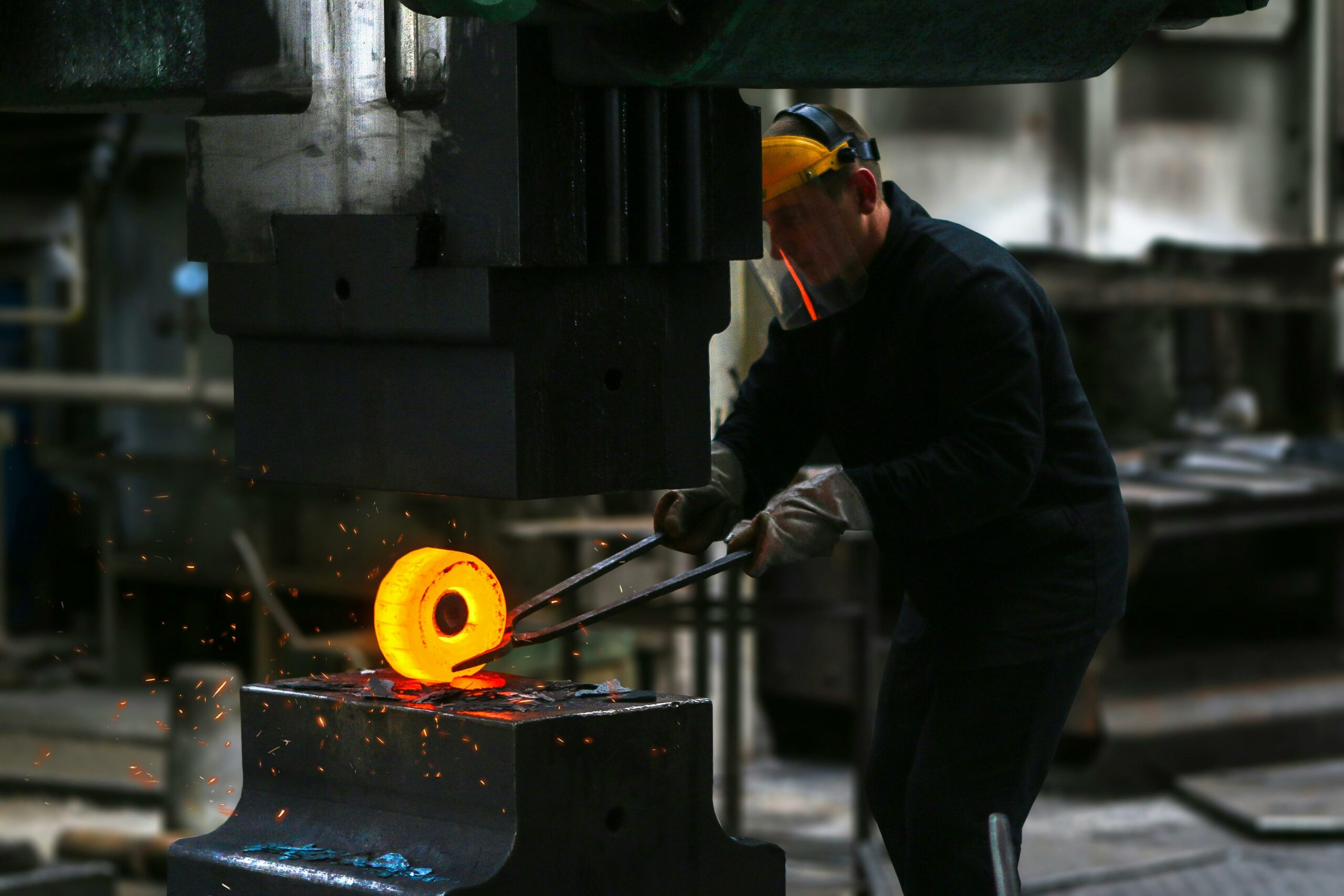 A blacksmith skillfully working with red-hot metal in an industrial setting, showcasing craftsmanship.